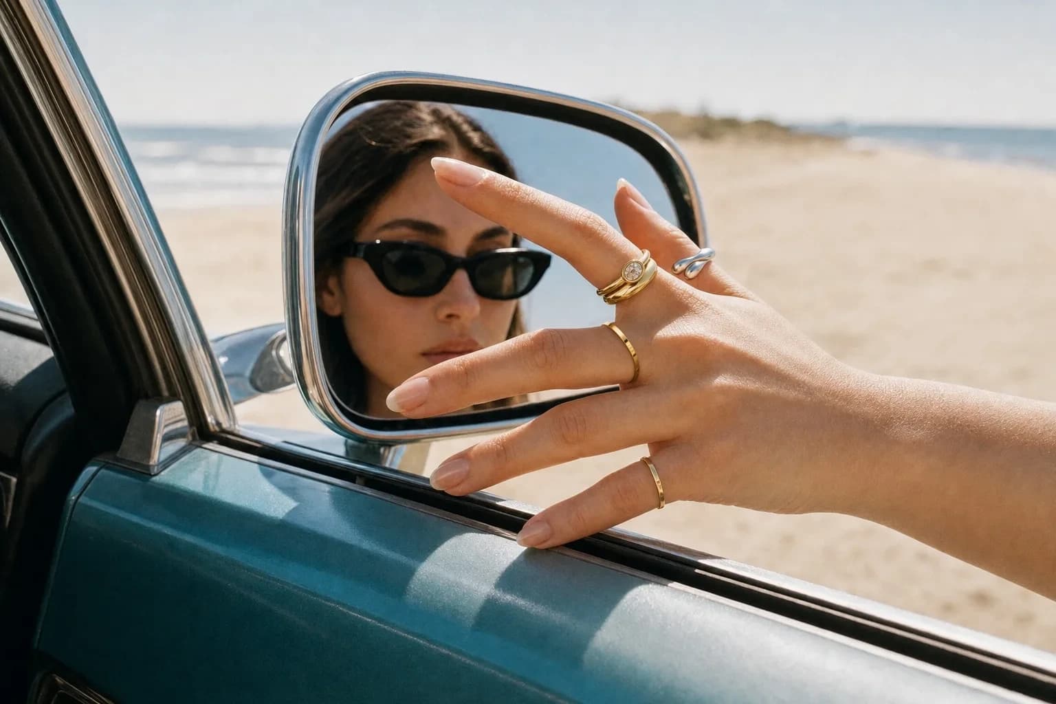 A hand at a car mirror by the beach wearing the Luna Orbit, Molten Wave, Serenity Band and Drift Wave rings