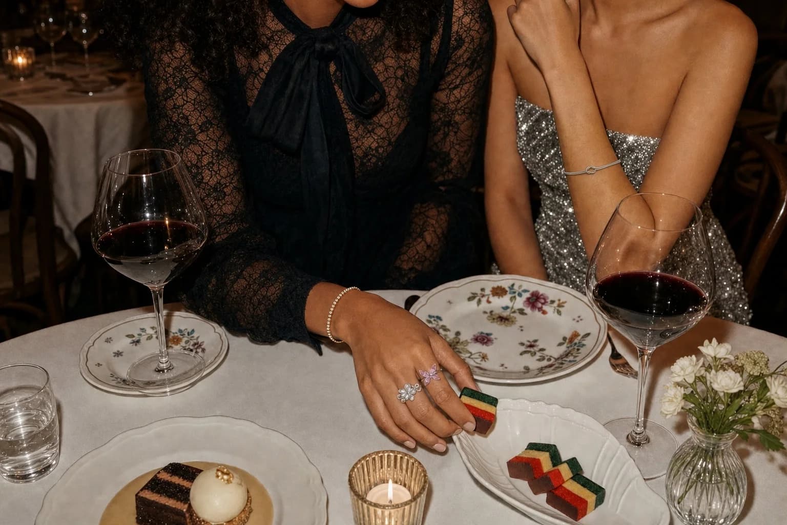 Dinner with friends, a hand wearing the Petal Crown and Blush Flutter rings with the Knot Bangle and Crystal Tennis Bracelet