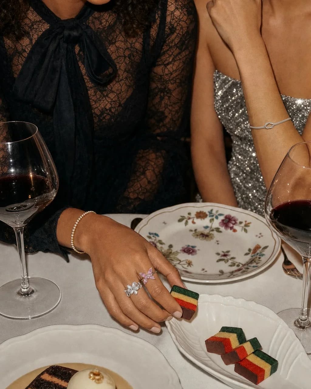 Dinner with friends, a hand wearing the Petal Crown and Blush Flutter rings with the Knot Bangle and Crystal Tennis Bracelet