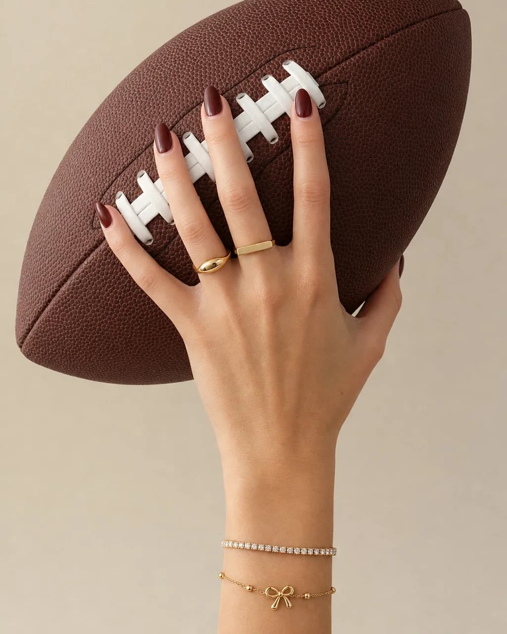 A hand gripping a football, wearing the Molten Wave and Horizon rings with a Crystal Tennis Bracelet and a Bow Knot Bracelet