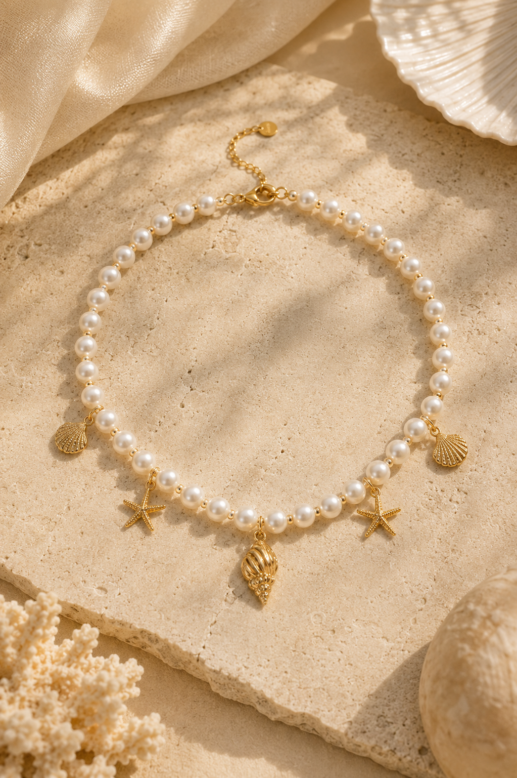 Pearl necklace with shell, star fish pendant and gold charms on a sandy surface