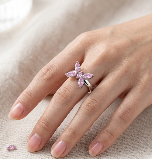 Hand wearing a pink butterfly ring on a neutral background