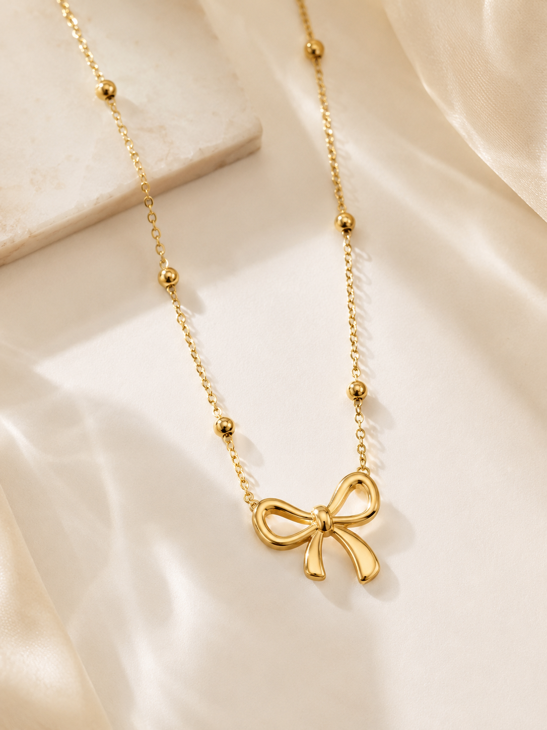 Gold bow,shaped necklace on a soft beige fabric background