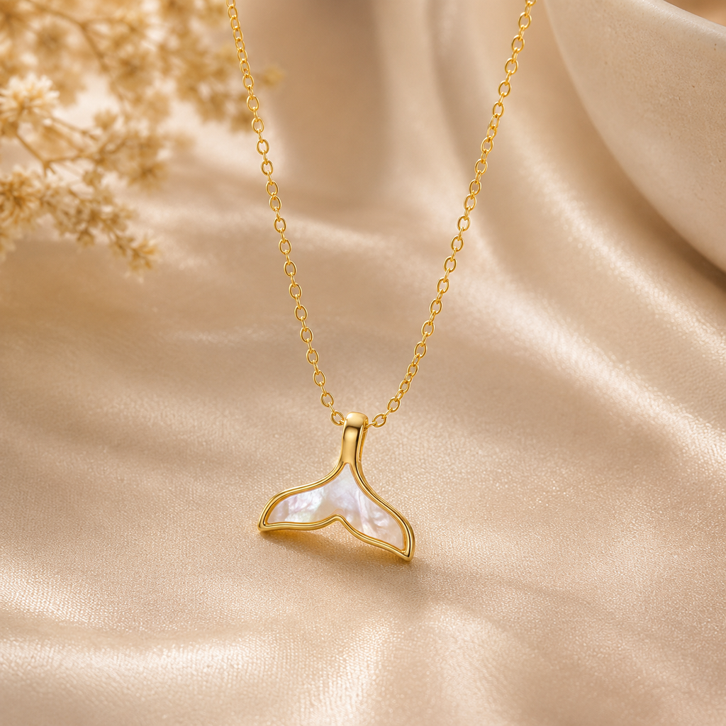 Gold necklace with a whale tail pendant on a beige fabric background