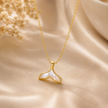 Gold necklace with a whale tail pendant on a beige fabric background