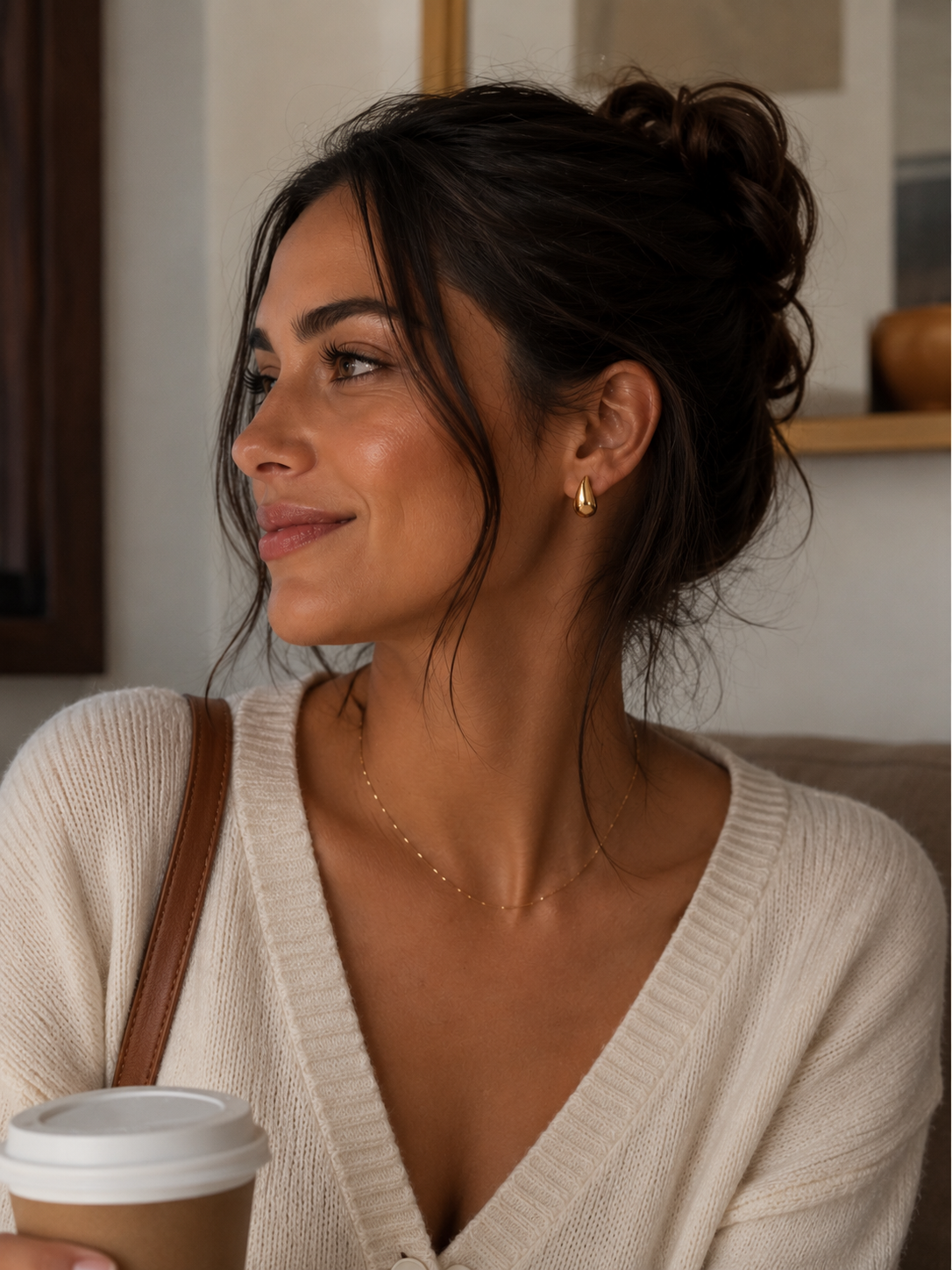 Woman holding a coffee cup indoors, wearing a beige sweater.