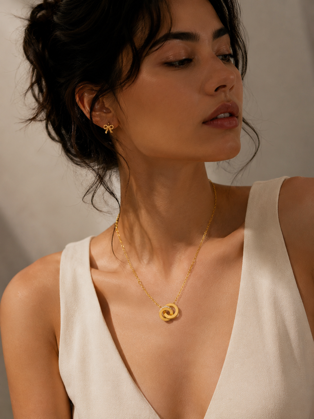 Woman wearing a gold necklace and earrings against a neutral background