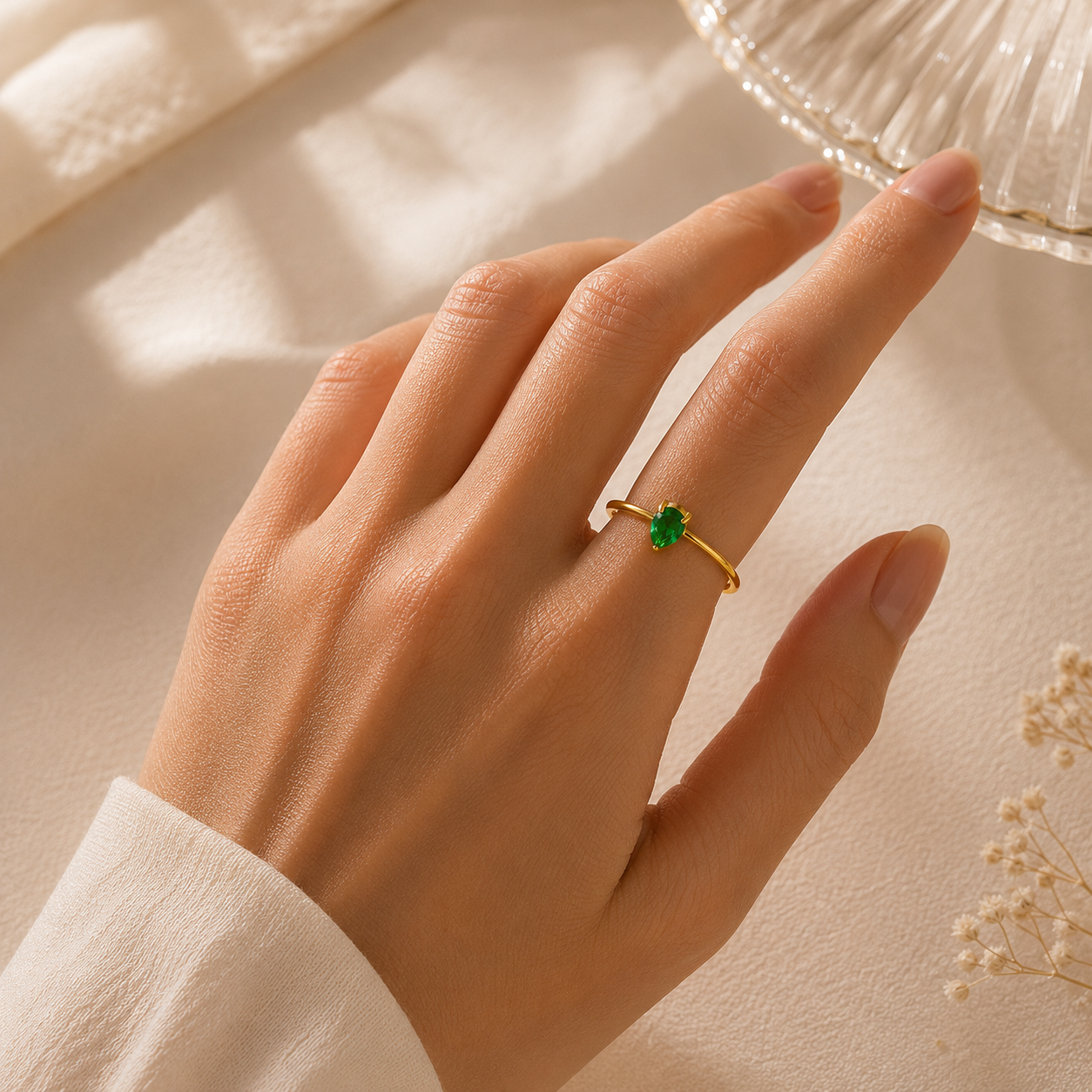 Hand wearing a gold ring with a green gemstone on a neutral background
