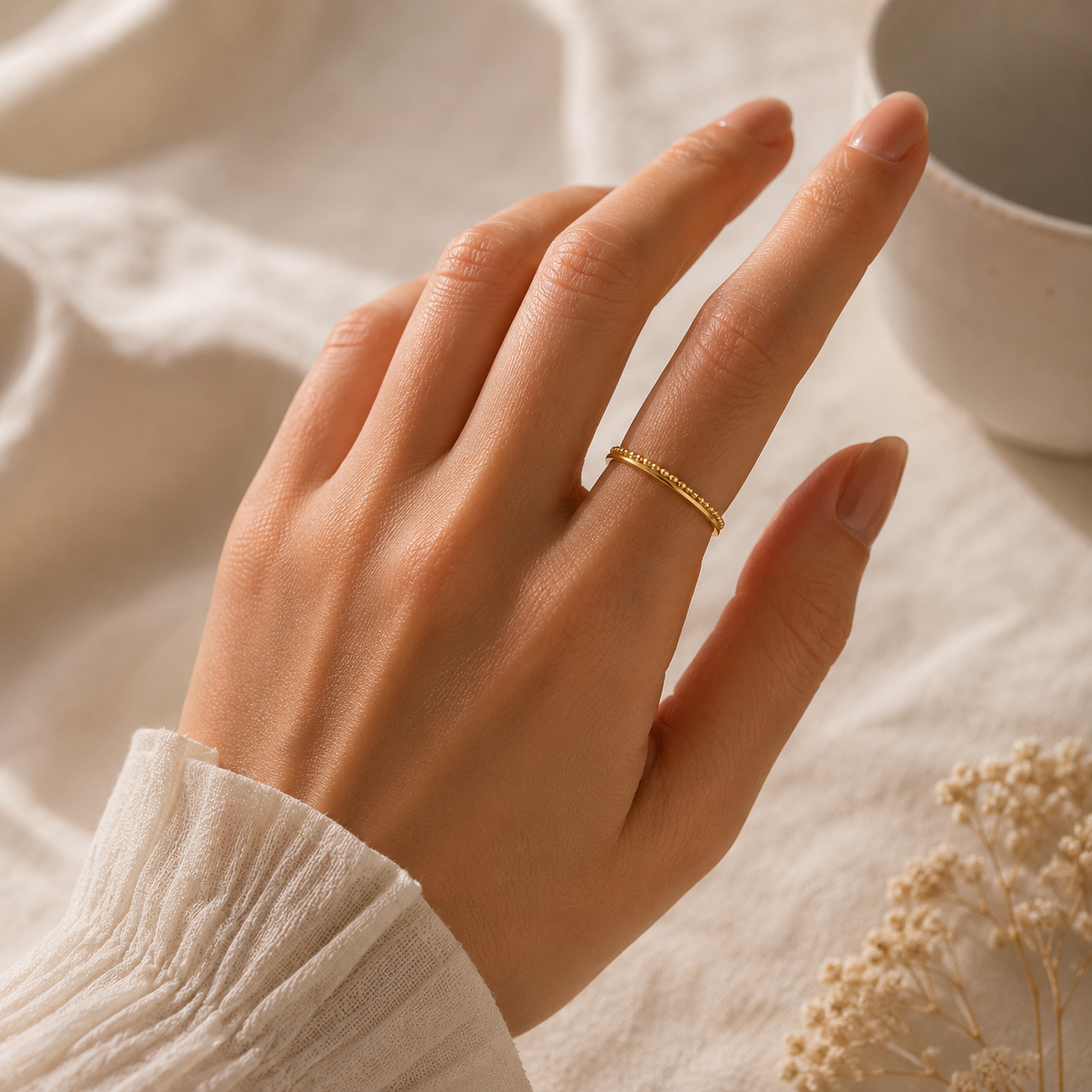 Hand wearing a gold ring on a soft, golden beaded band