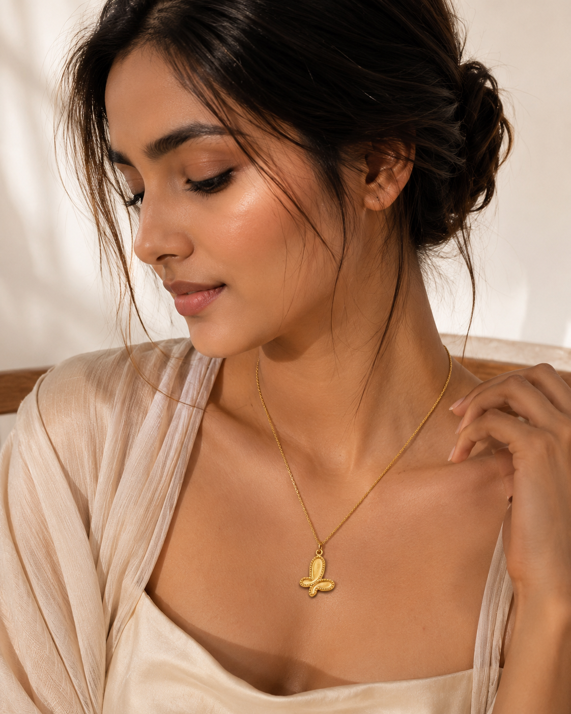 Woman wearing a gold necklace with a butterfly pendant against a neutral background