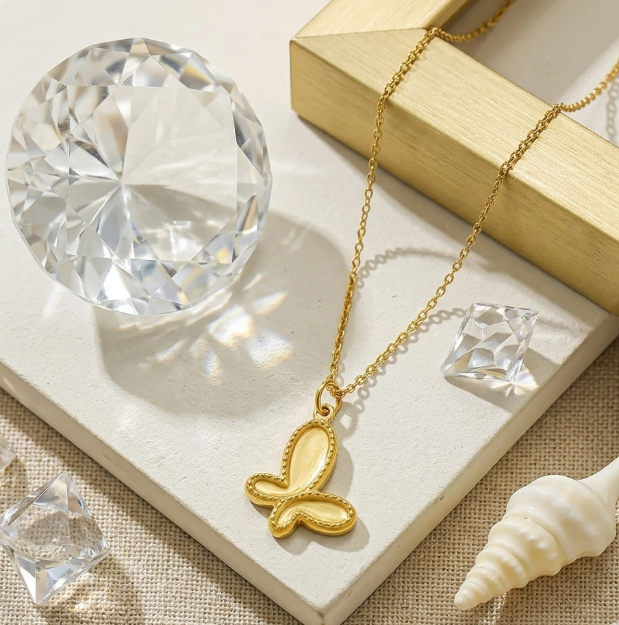 Gold butterfly necklace with clear crystal pendant on a beige surface