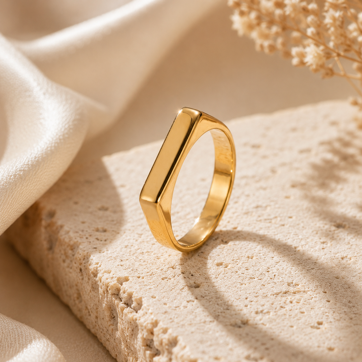 Gold ring on a textured beige surface with fabric and dried flowers