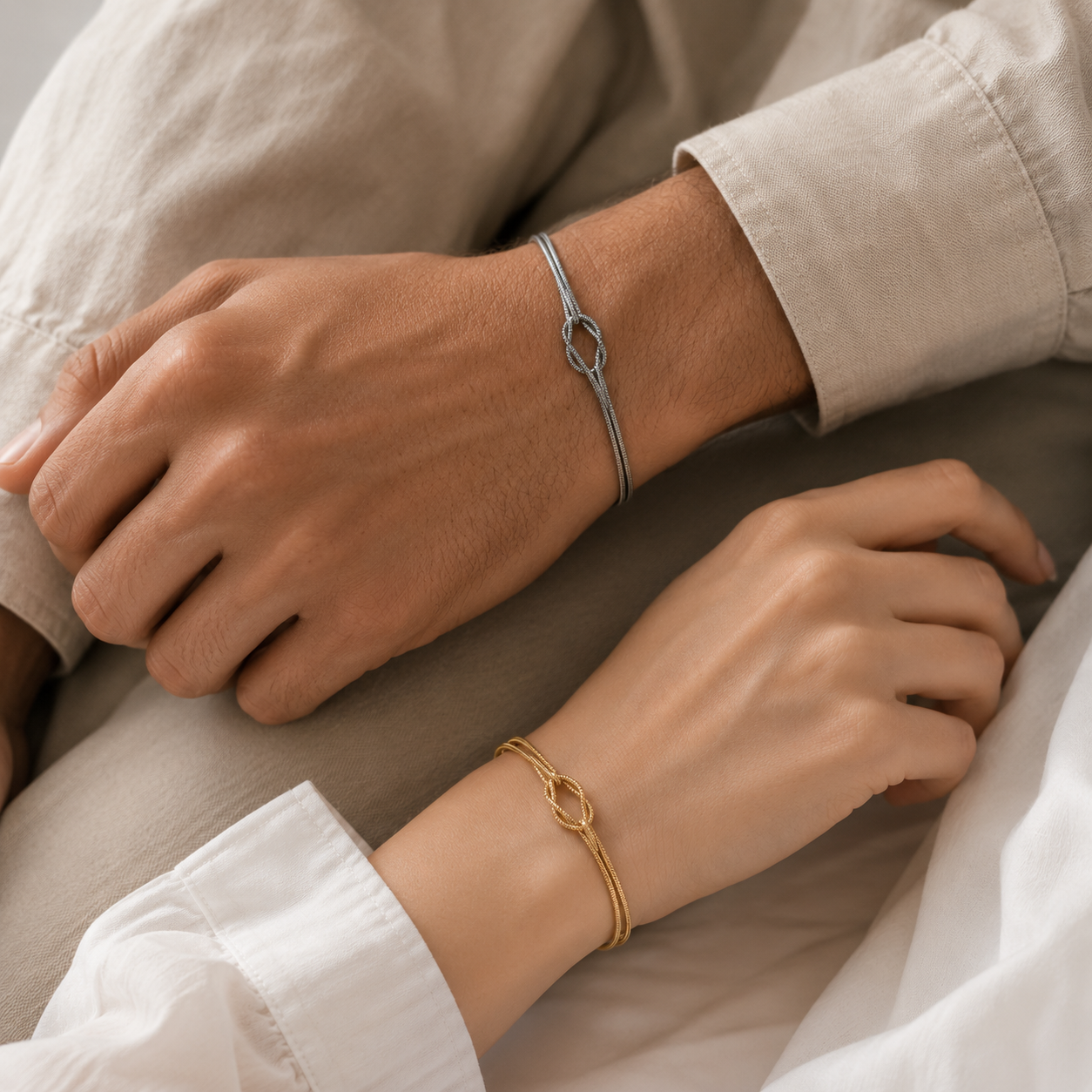 Man and woman wrists wearing silver and gold bracelets on a neutral background
