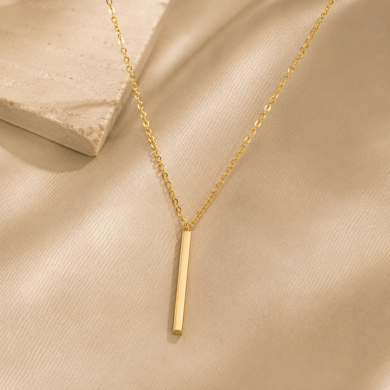 Gold necklace with a vertical bar pendant on a beige fabric background