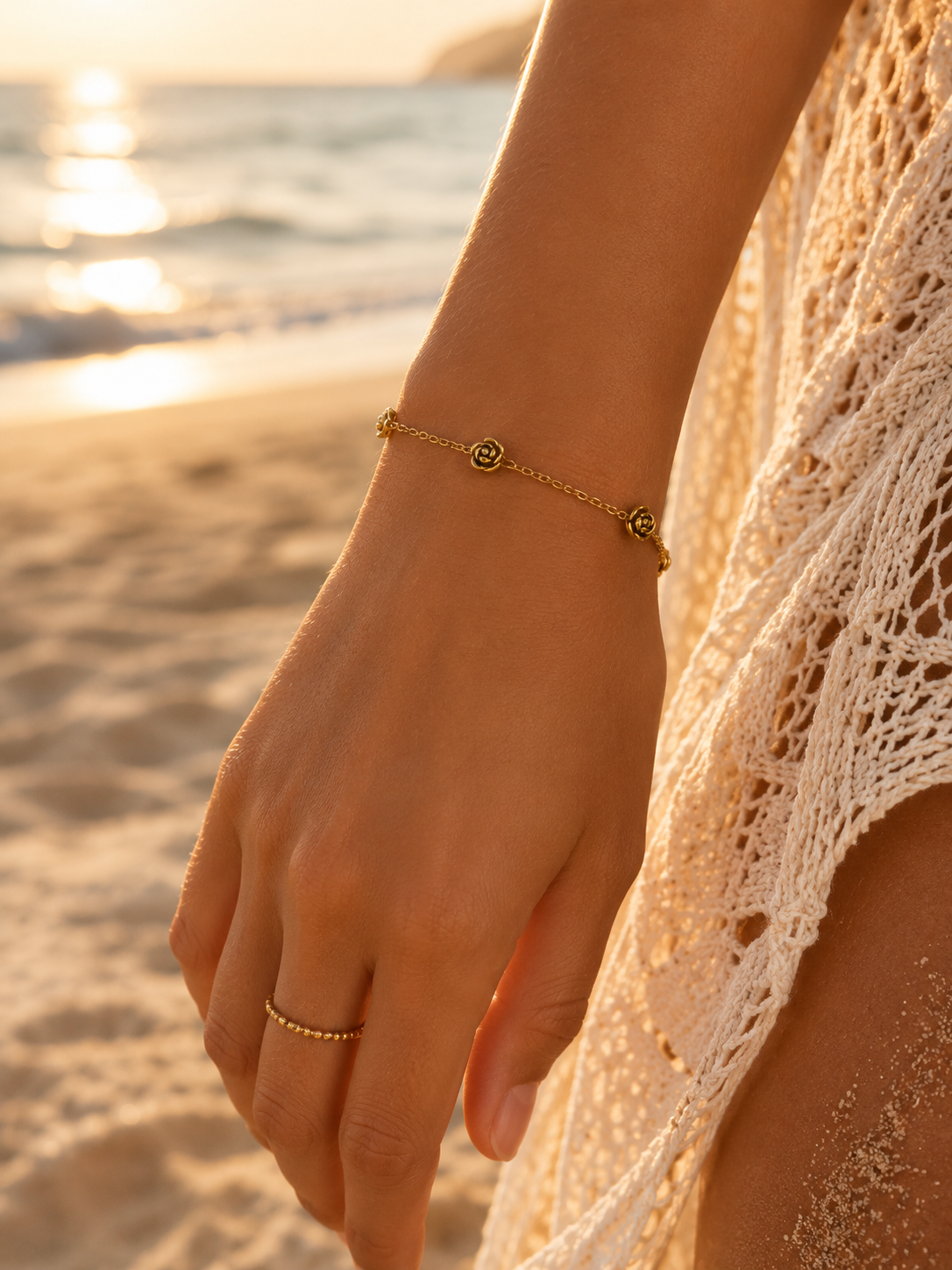 Hand wearing a gold bracelet on a beach with sunset in the background