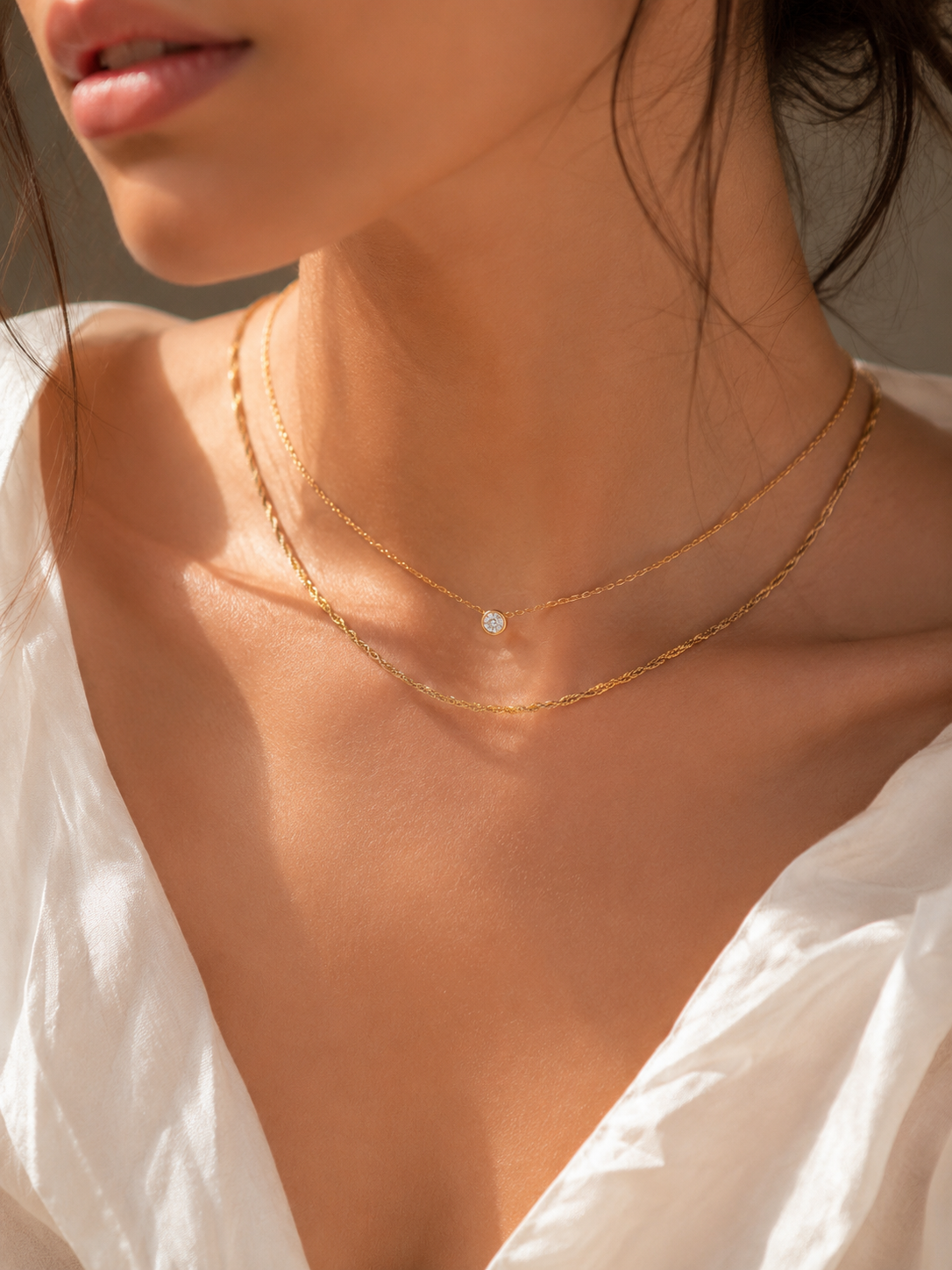 Close,up of a person wearing a delicate gold necklace with a small diamond pendant.