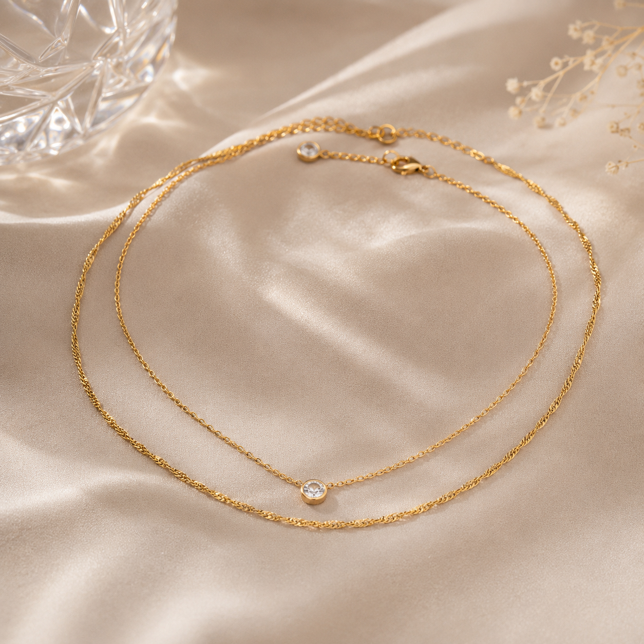 Two gold necklaces with small gemstones on a beige fabric background